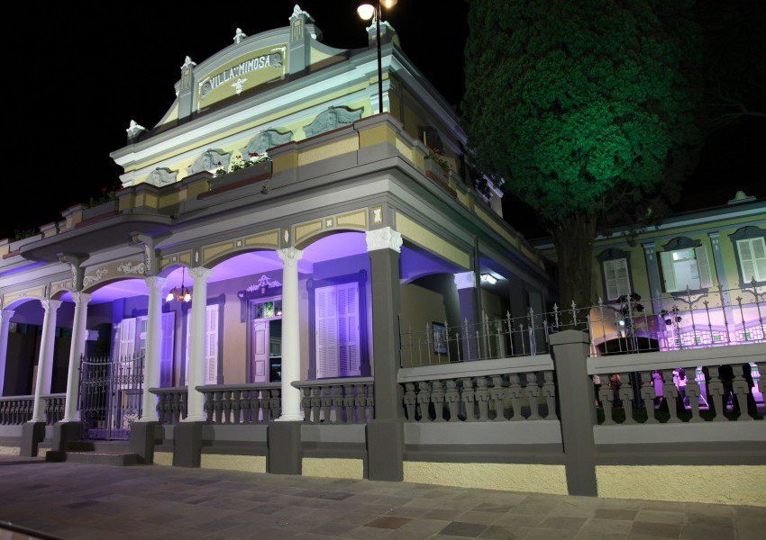 Foto que ilustra matéria sobre o que fazer em Canoas mostra a fachada da Casa das Artes Villa Mimosa iluminada à noite.