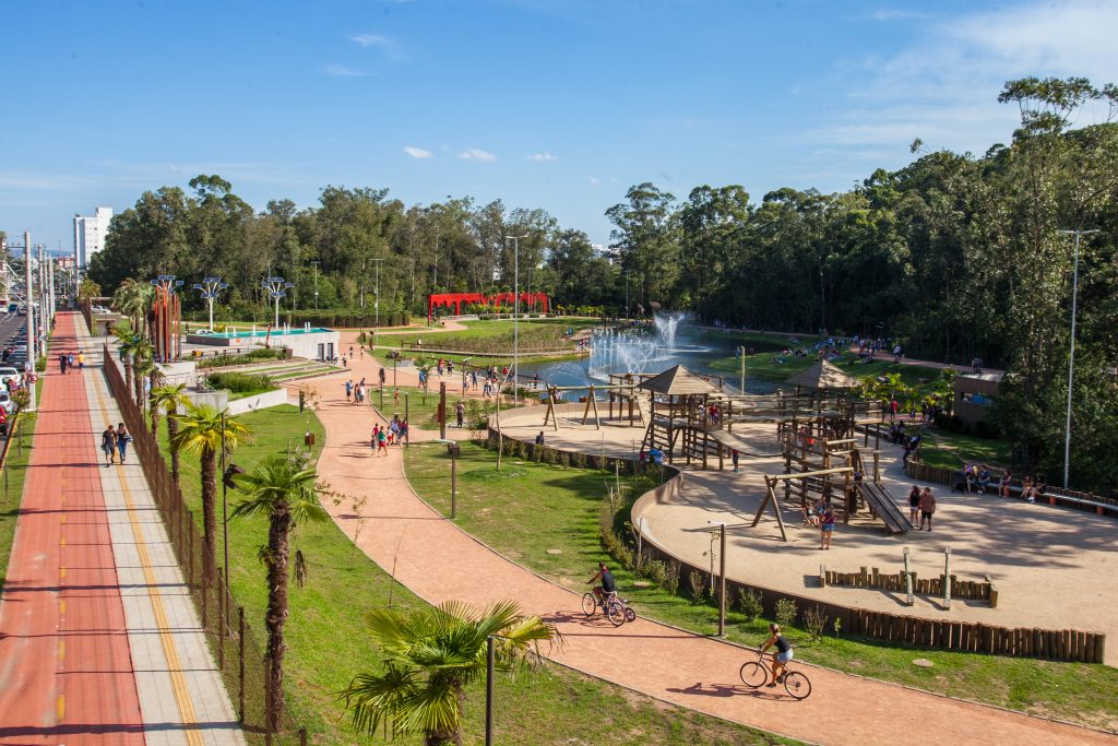 Foto que ilustra matéria sobre o que fazer em Canoas mostra uma imagem vista do alto do Parque Getúlio Vargas, com playground, pistas para caminhada e bicicletas, um pequeno lago e muitas árvores ao lado. 