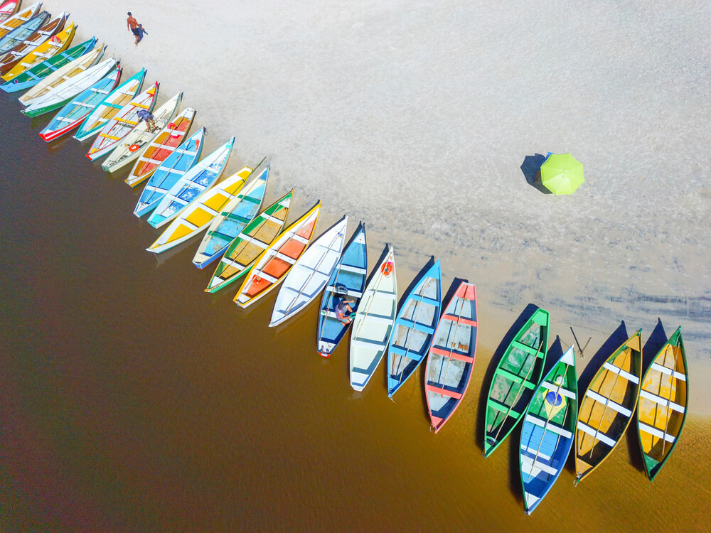 Foto que ilustra matéria sobre o que fazer em Palhoça mostra uma série de barquinhos coloridos à beira do rio que corre ao lado da praia da Guarda do Embaú