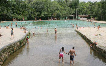 Foto que ilustra matéria sobre parques em Brasília mostra a entrada de uma das piscinas do Parque Nacional de Brasília, repleta de pessoas se banhando e com várias árvores ao fundo.