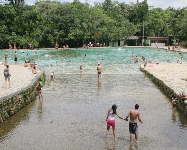 Foto que ilustra matéria sobre parques em Brasília mostra a entrada de uma das piscinas do Parque Nacional de Brasília, repleta de pessoas se banhando e com várias árvores ao fundo.