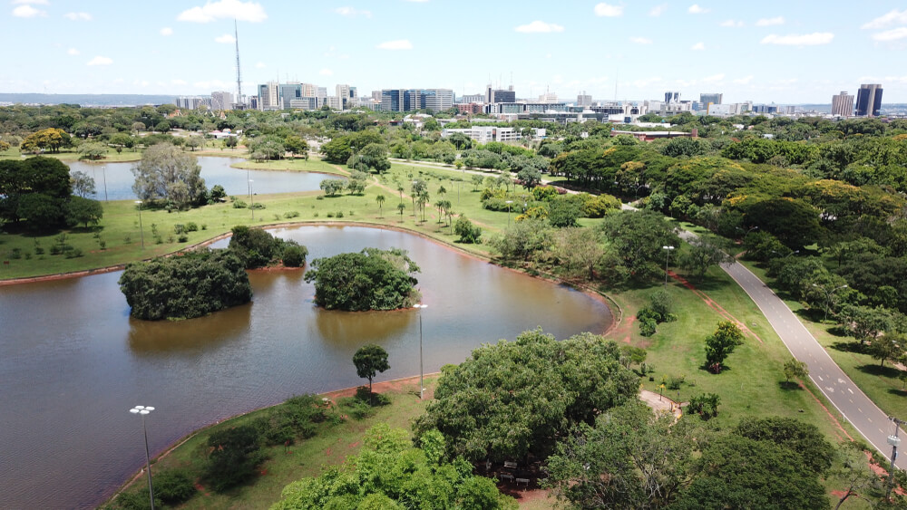 Foto que ilustra matéria sobre Parques em Brasília mostra uma imagem do alto do Parque da Cidade Dona Sarah Kubitschek, onde aparecem dois lagos, muitas árvores e uma pista de corrida que também serve como ciclovia. Ao fundo, os prédios da cidade.