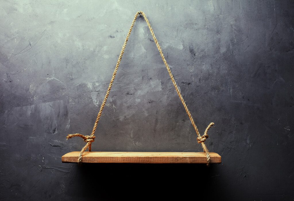 Foto de uma prateleira pendurada em uma parede por meio de corda. A corda e a madeira formam um triângulo.