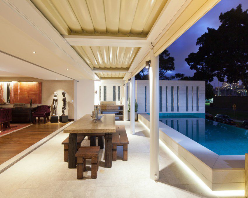 Área gourmet externa com piscina, iluminação amarela e mesa de madeira ao centro. Imagem disponível em Pexels
