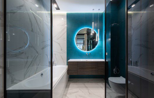 Foto de um banheiro moderno com banheira, espelho redondo, pia com armário embutido e vaso sanitário.