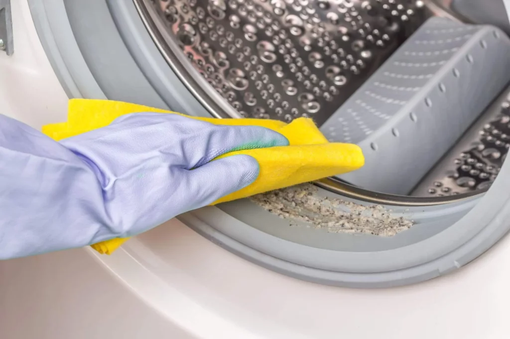  Imagem de uma pessoa limpando a borracha de vedação de uma máquina com uma flanela amarela para ilustrar matéria sobre como limpar máquina de lavar com abertura frontal

