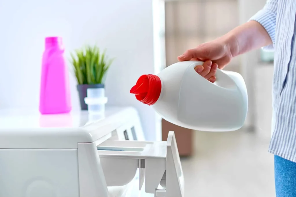 Imagem de uma mulher colocando um produto dentro de uma máquina para ilustrar matéria sobre como limpar máquina de lavar com água sanitária