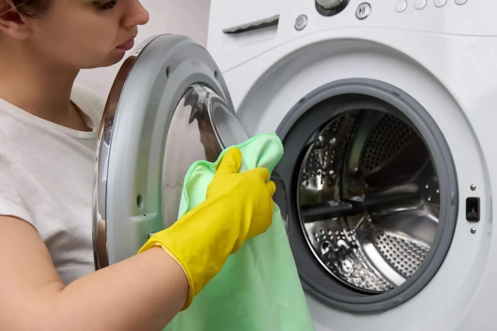 Imagem de uma mulher limpando uma máquina com uma flanela seca para ilustrar matéria sobre como limpar máquina de lavar por fora