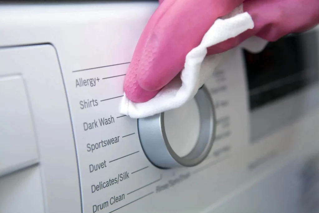 Imagem de uma pessoa com luva rosa limpando a parte externa de uma máquina com uma flanela branca para ilustrar matéria sobre como limpar máquina de lavar por fora
