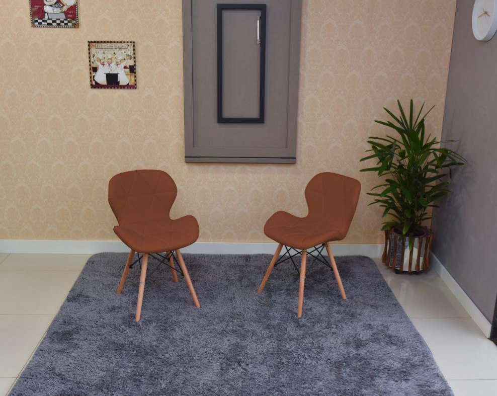 Foto de um exemplo de uma sala de jantar em um apartamento pequeno decorado. A imagem mostra a mesma mesa da imagem anterior, mas agora ela está recolhida na parede. O contexto é o mesmo: duas cadeiras, quadros decorativos, um relógio de parede e um tapete.