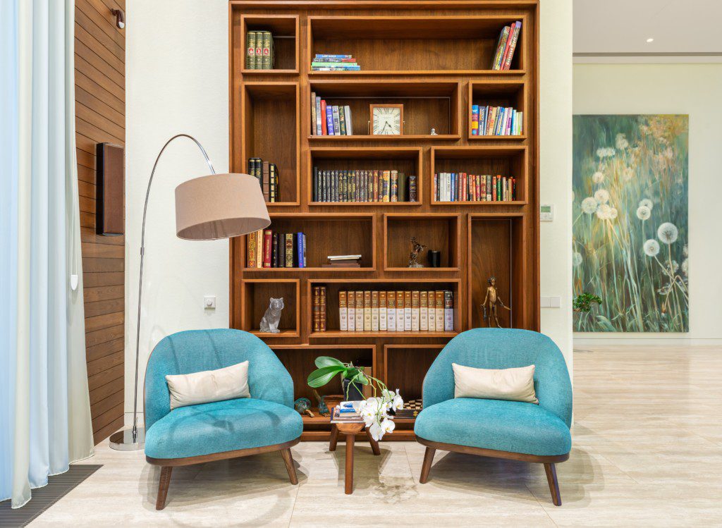 A foto mostra um exemplo de decoração retrô no cantinho de leitura com duas poltronas azuis, uma luminária de chão e uma estante de livros.