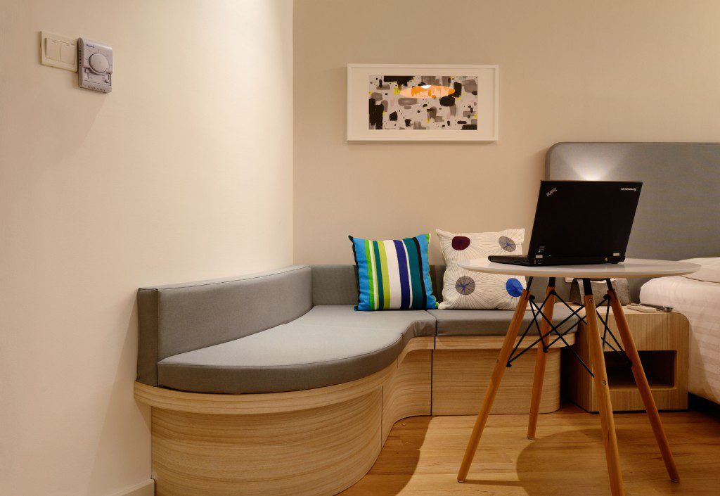 A foto mostra um exemplo de decoração retrô no quarto com um sofá em curvas, mesa com pés de palito, almofadas coloridas e quadro decorativo. 