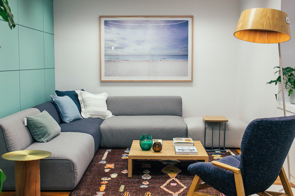 A foto mostra um exemplo de decoração retrô na sala de estar com um sofá em L, mesa de centro, poltrona, luminária de chão e quadro decorativo.