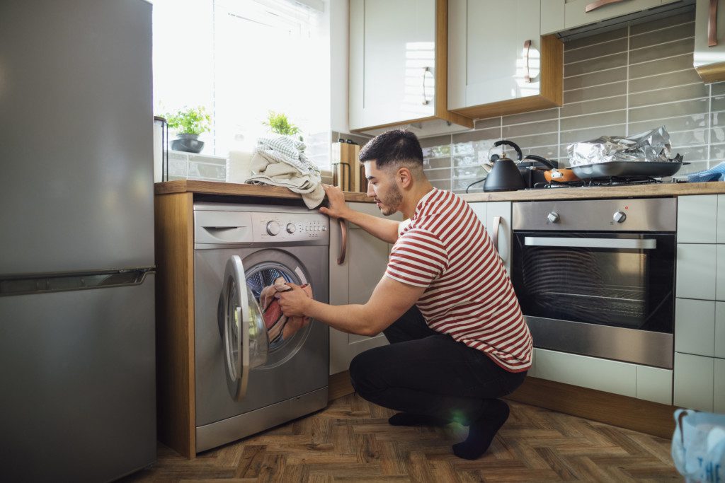 foto que ilustra matéria sobre cozinha com lavanderia mostra um homem abaixado colocando roupa para lavar