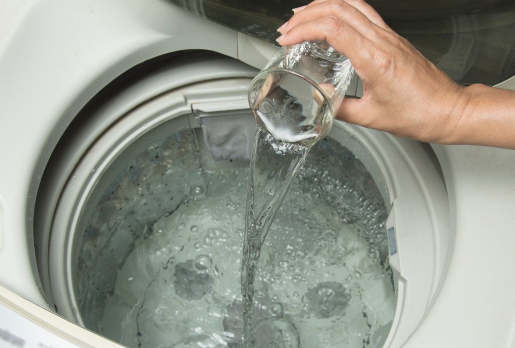 Foto que ilustra matéria sobre como limpar máquina de lavar mostra uma pessoa adicionando vinagre na máquina de lavar