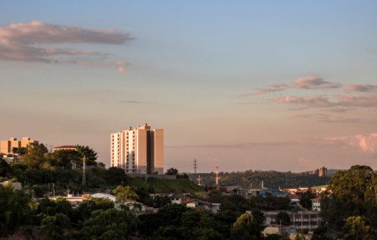 Foto que ilustra matéria sobre onde fica Várzea Paulista mostra uma vista panorâmica da cidade no cair da tarde, com várias árvores e um prédio alto que se destaca no centro da imagem.