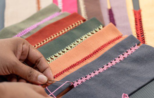 Imagem de um tecido sendo bordado a mão.