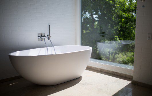 Imagem de banheira de cerâmica branca ao lado de uma parede de vidro.