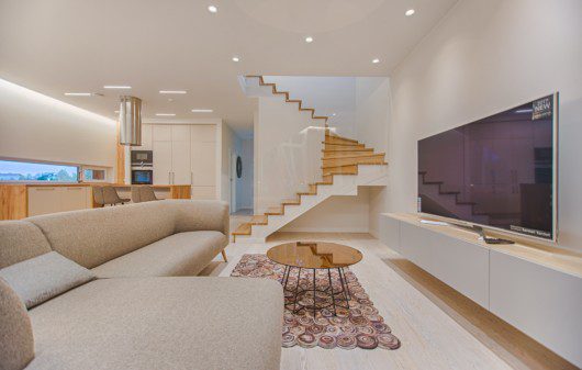 Imagem de uma sala de estar com decoração moderna na cor branca com detalhes em madeira.