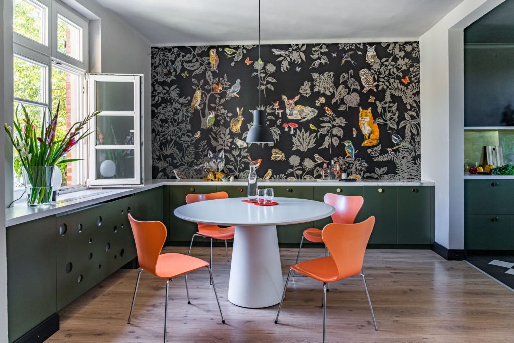 Sala de jantar colorida, com papel de parede com desenhos de plantas e animais.