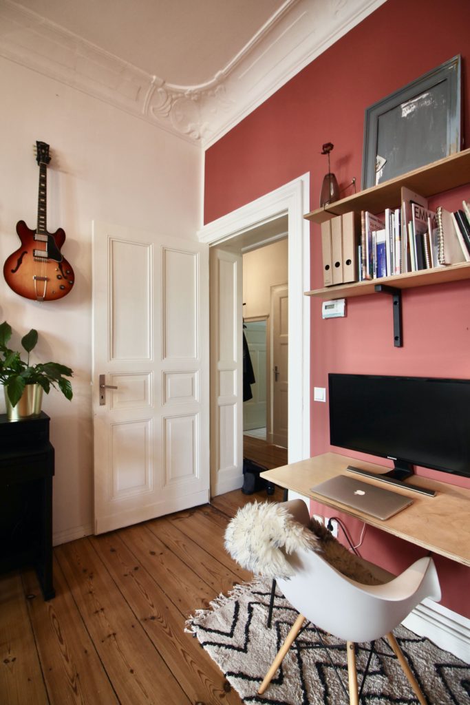 Escritório com parede rosa e móveis brancos.