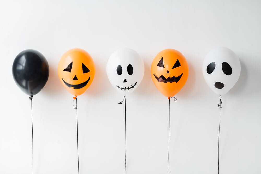 Foto que ilustra matéria sobre decoração de Halloween mostra balões nas cores preta, laranja e branco, com caras sorridentes e assustadoras. 