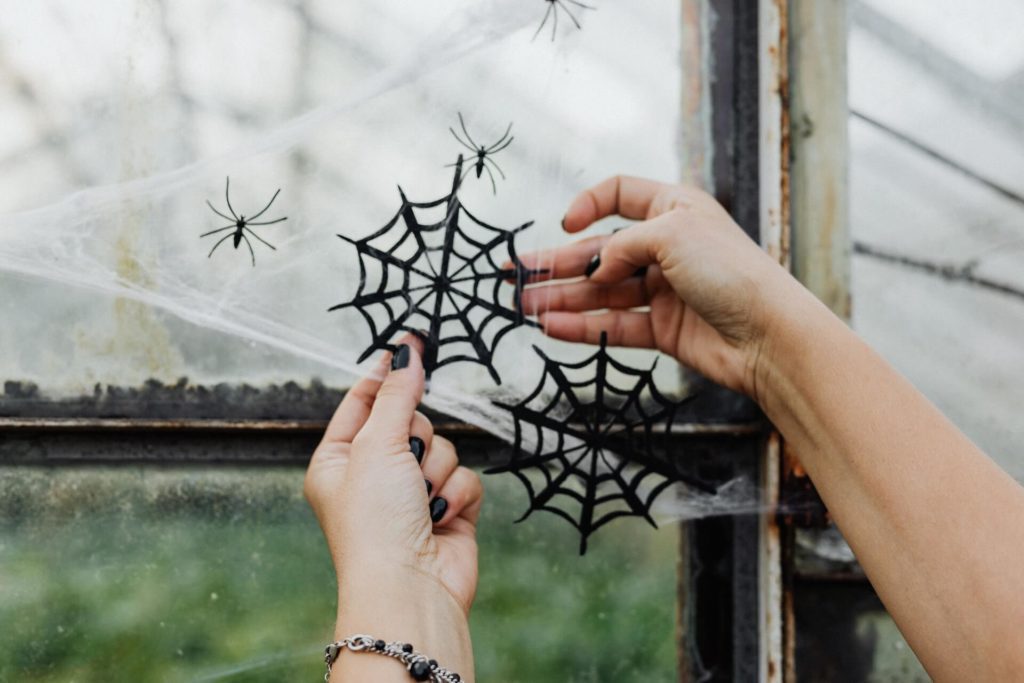 Foto que ilustra matéria sobre decoração de Halloween mostra mãos arrumando uma teia de aranha falsa para decorar