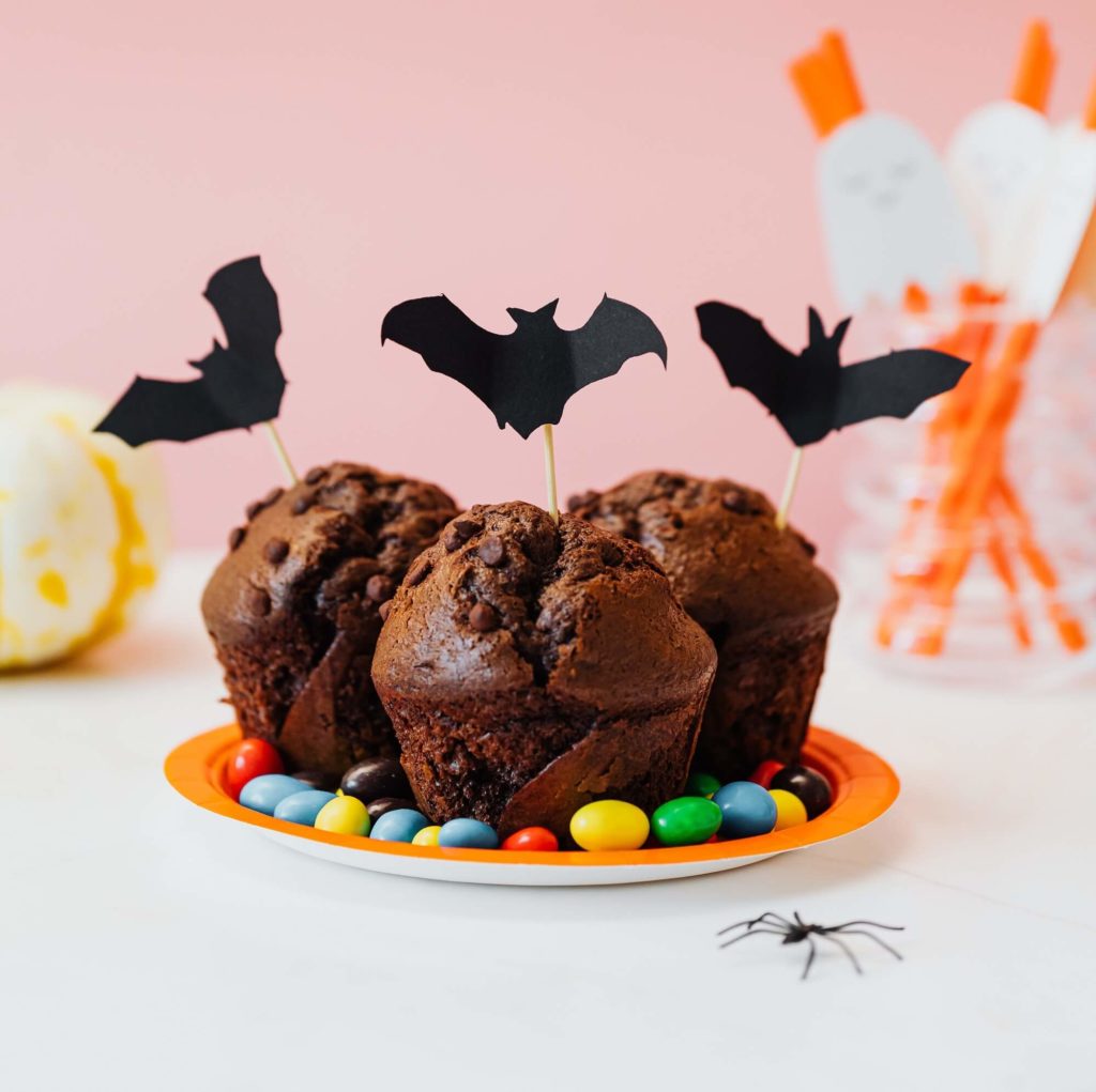 Foto que ilustra matéria sobre decoração de Halloween mostra um prato com três pequenos bolos de chocolate com morcegos de papel espetados neles.