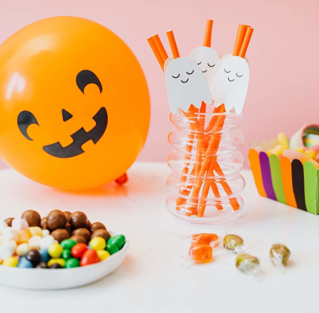 Foto que ilustra matéria sobre decoração de Halloween mostra uma bola de encher laranja com uma cara sorridente e canudos com fantasminhas grudados. 