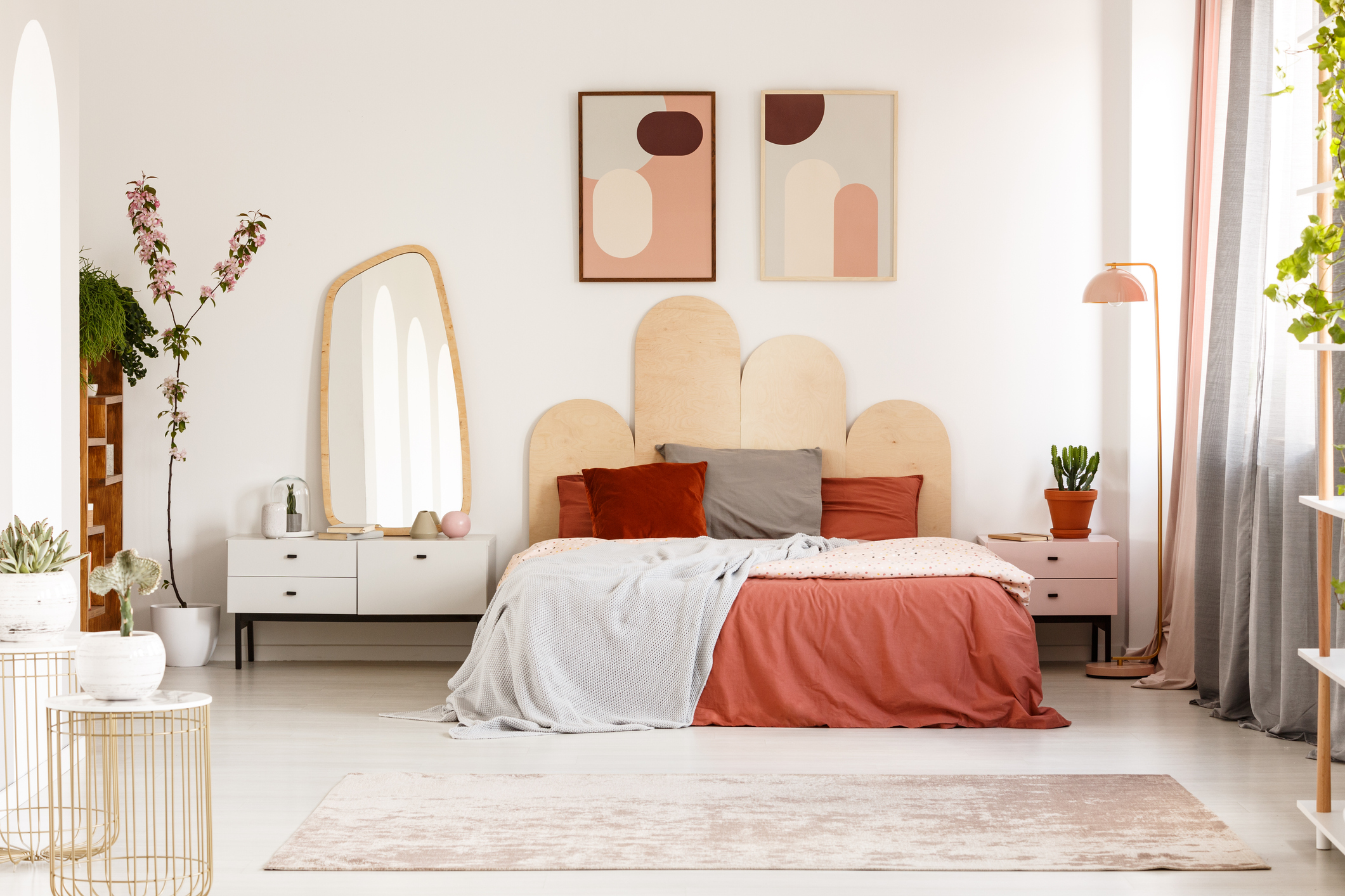Imagem de um quarto em tons terrosos e rosa com cabeceira arredondada e espelho com moldura em madeira. 