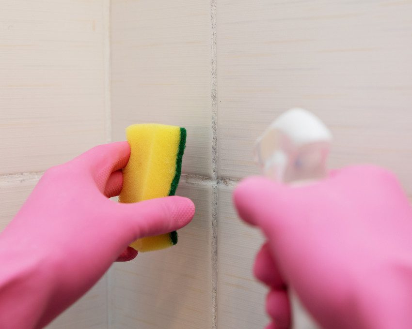 Imagem de uma pessoa limpando azulejo de um banheiro com esponja.