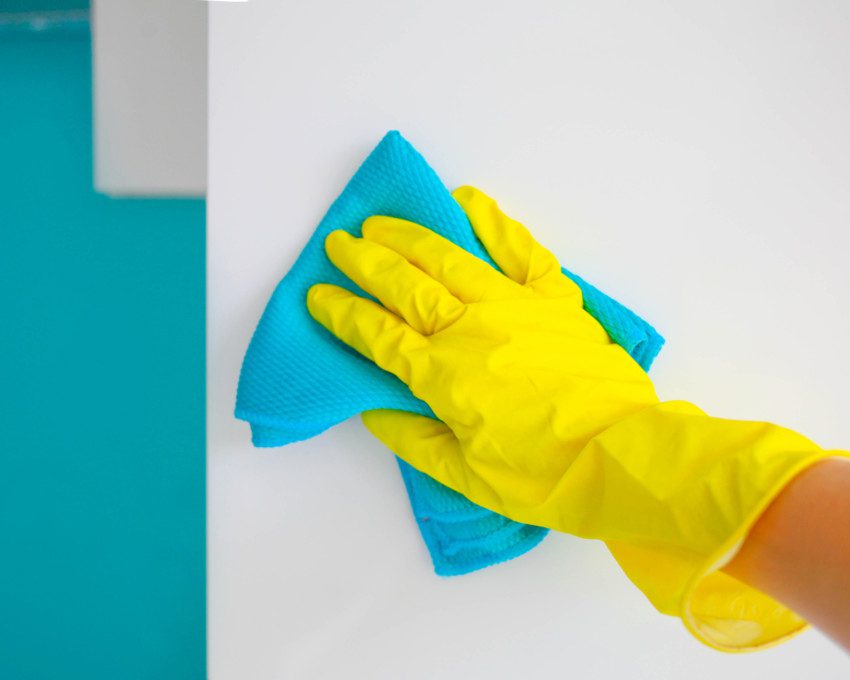 Imagem de uma pessoa limpando uma parede com luvas de borracha e uma esponja.