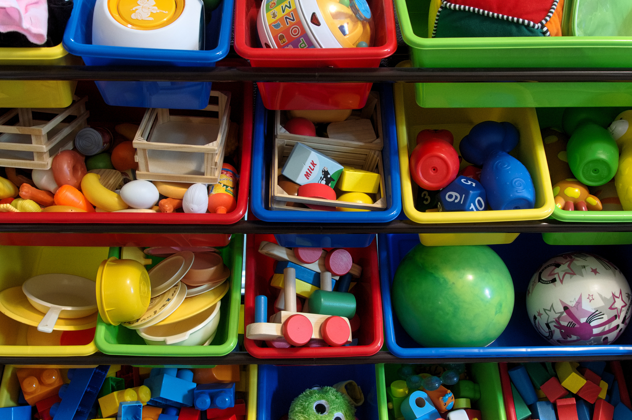 Imagem de brinquedos de criança organizados em caixas de plástico coloridas.
