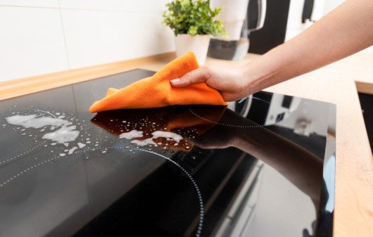 Imagem de uma pessoa limpando um fogão cooktop.