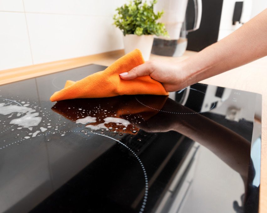 Imagem de uma pessoa limpando um fogão cooktop.