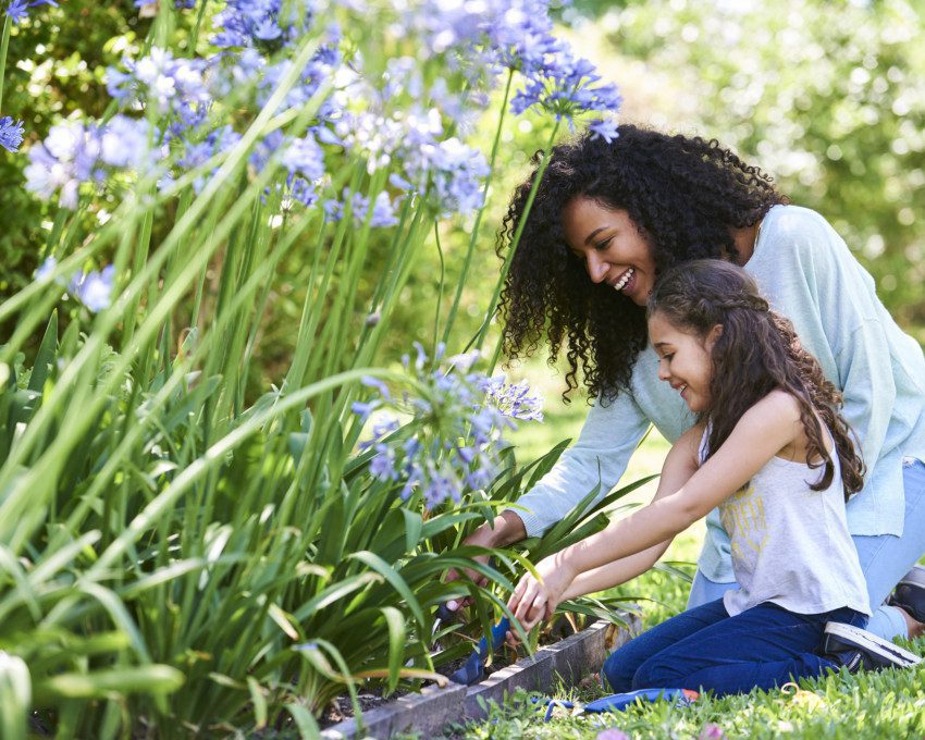 Foto que ilustra matéria sobre jardim no quintal mostra uma mulher e uma criança plantando em um jardim no quintal