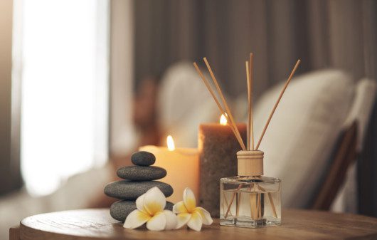 Imagem de um aromatizador de ambiente, velas, pedras e duas flores.