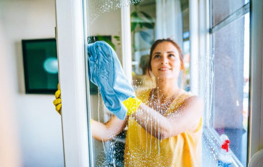 Imagem de uma mulher limpando uma janela de vidro.