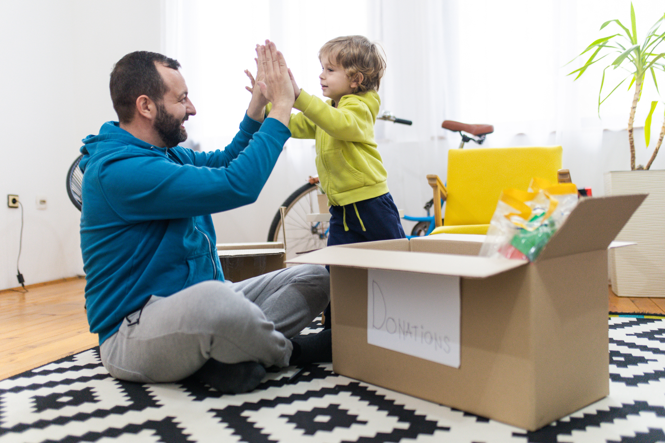 Imagem de um pai e filho se cumprimento ao lado de uma caixa de papelão com brinquedos para doação.