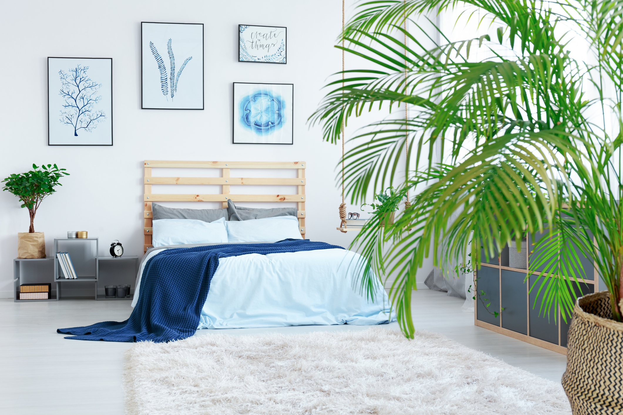 Imagem de um quarto despojado com plantas, detalhes em azul e cabeceira em pallet.