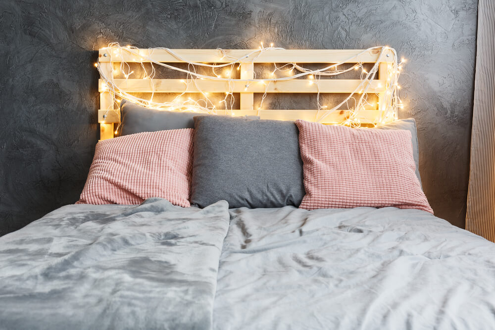 Foto que ilustra matéria com ideias de cabeceira mostra uma cama com uma cabeceira feita com palete e pequenas luzes penduradas nela.