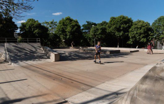 Foto que ilustra matéria sobre parque em Contagem mostra a pista de skate do Parque das Amendoeiras, onde aparece um menino andando. Ao fundo, muitas árvores e um céu azul em um dia claro.