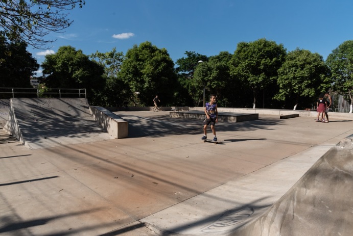 Foto que ilustra matéria sobre parque em Contagem mostra a pista de skate do Parque das Amendoeiras, onde aparece um menino andando. Ao fundo, muitas árvores e um céu azul em um dia claro.