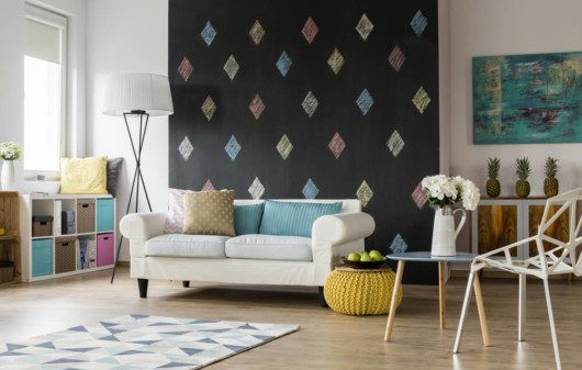 Foto que ilustra matéria sobre pinturas diferentes de parede mostra uma sala de estar com uma parede inteira de lousa, com losangos pintados com diferentes cores de giz.