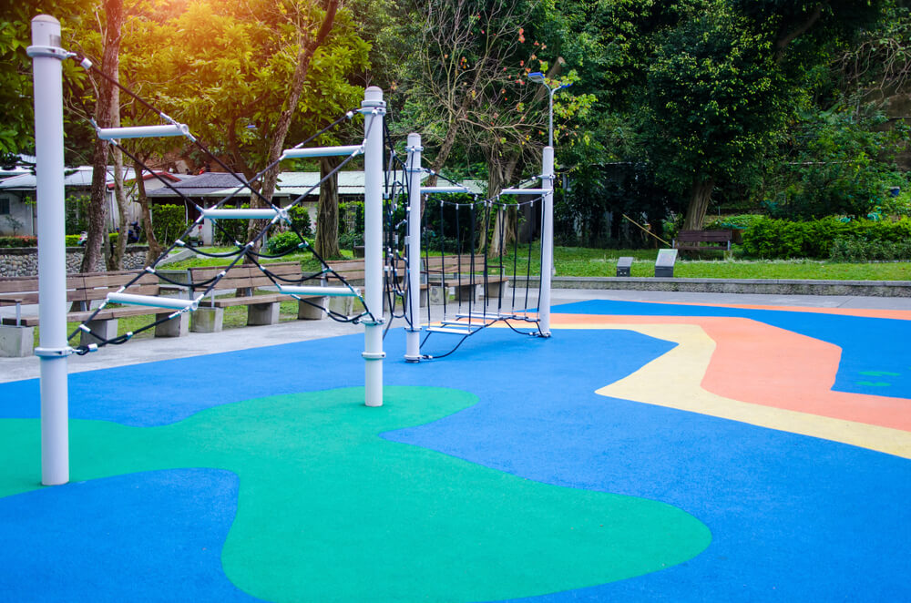 Foto que ilustra matéria sobre tipos de piso mostra uma área externa de playground com um piso emborrachado colorido.