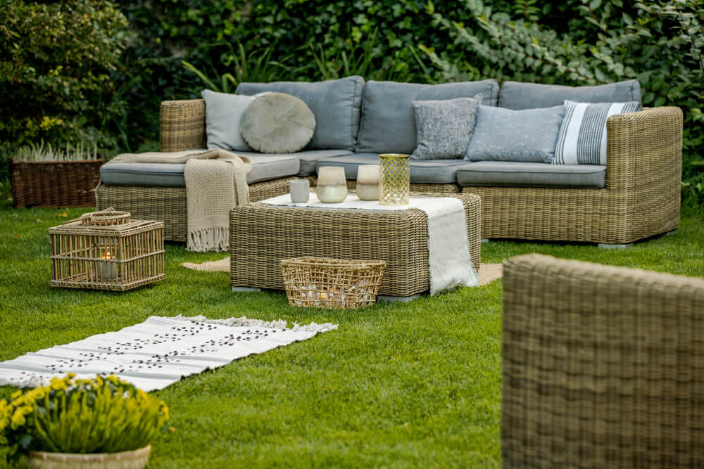Foto que ilustra matéria sobre tipos de piso mostra uma área externa de jardim toda gramada, com sofás repletos de almofadas, e pufes.