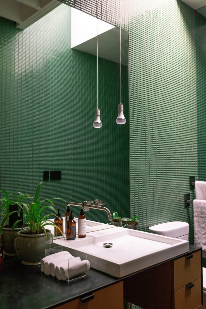 Lavabo com parede de cerâmica verde e lâmpada pendente. Imagem disponível em Pexels.