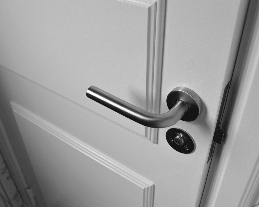 Imagem que ilustra matéria sobre tipos de fechadura mostra uma fechadura de alumínio em uma porta branca que está fechada.