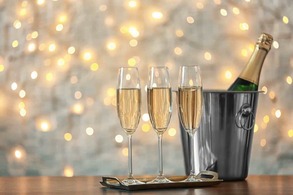 Foto que ilustra matéria sobre decoração de Ano Novo mostra três taças cheias de espumante à frente de um balde de inox com uma garrafa fechada;