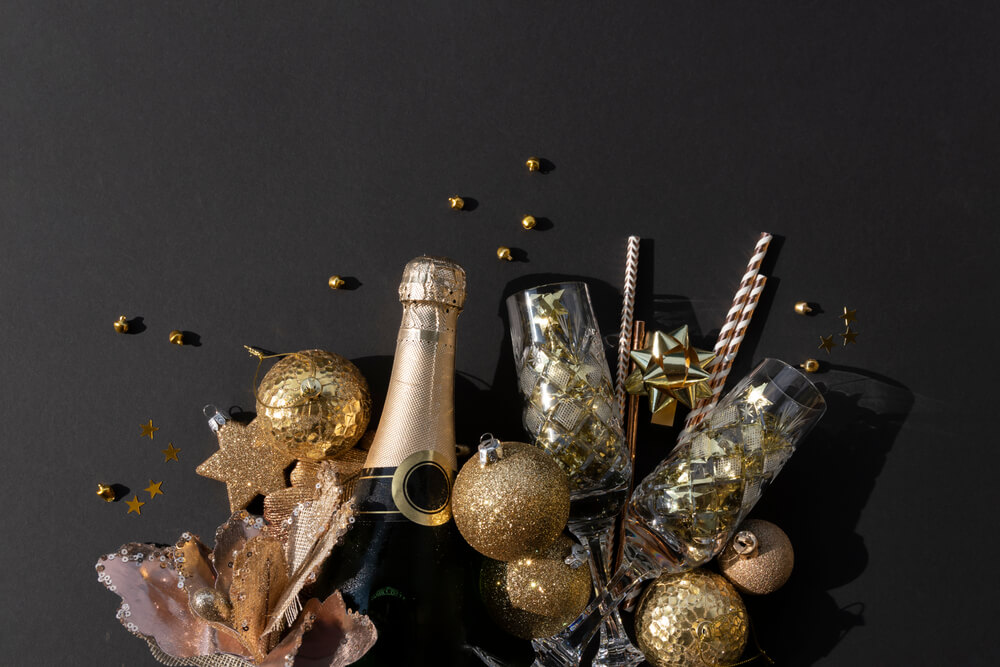 Foto que ilustra matéria sobre decoração de Ano Novo mostra enfeites de Natal, como bolas de árvores e estrelas, juntos de uma garrafa de espumante e duas taças.